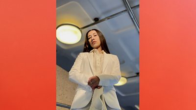 Nicole Petrus Barracks stands staring into camera. It's a three-quarter length shot and she's wearing a full white suit. She has straightened her hair,  