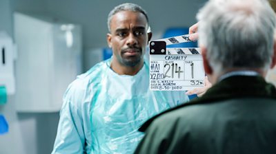 Behind the scenes filming on the set of Casualty, showing actor Charles Venn in scrubs standing behind a clapperboard