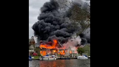 Fire burns at a boatyard on a River Thames island