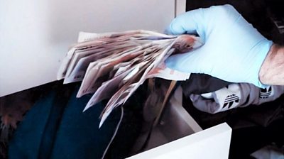 A gloved hand holds UK bank notes