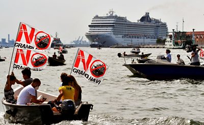 Protesters in a boat in front of the cruise ship, with signs that read 'no big ships.'