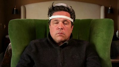 Comedian and travel writer Dom Joly has his eyes closed. He is wearing a URGOnight device on his head