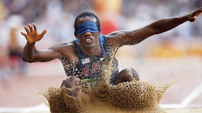 Lex Gillette landing in the sand from a long jump