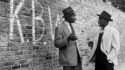 1952: Two Jamaican men talking in a street in Brixton, south London. The graffiti on the wall stands for 'Keep Britain White'. 