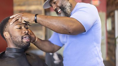 A young black man gets his haircut by a barber
