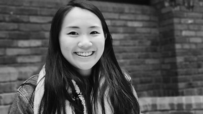 Black and white photo of Vivian Young tight shot. Smiling to camera. Long hair passed shoulder. Outside with brick wall behind her. 