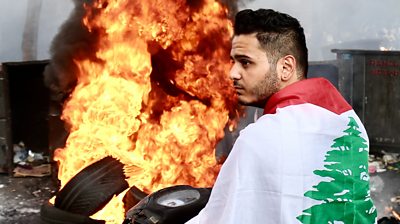 Person with Lebanese flag in front of burning tyres, 15 July 2021
