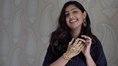 Jewellery designer Anisha Parmar wears an intricate gold hand chain in front of a wall