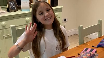 a-young-girl-called-daisy-sits-at-a-kitchen-table-and-waves