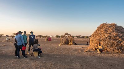 In northern Kenya, 鶹Լ Media Action crew films Lomilio, who lost nearly 1,000 goats in a flood. He sits in front of his thatched home.