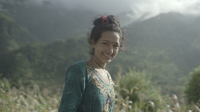 Nirmala Chanda, 19, is smiling at the camera. She is outdoors in the mountains of far western Nepal.