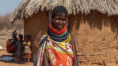 A woman in bright traditional clothing is shown outside her home in rural northern Kenya