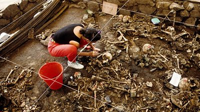 A woman examining bones in a mass grave