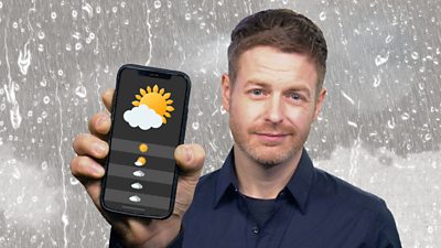 Weather presenter Tomasz Schafernaker holding up a mobile with a mock weather app on display