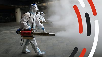 A person in a hazmat suit sprays disinfectant