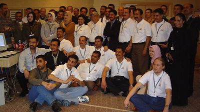 A group of people in white polo shirts with the orange Al Mirbad logo pose for a photograph in an office.