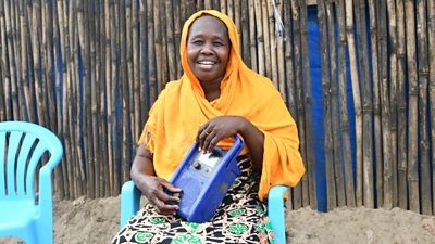 Mama Lia outside her home in Juba, with the radio she uses to listen to 'Let's Talk About Us'