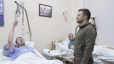 Volodymyr Zelensky in a hospital with soldiers lying on beds.