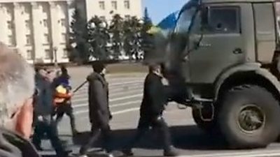 Civilians waving a Ukrainian flag in front of a Russian military vehicle