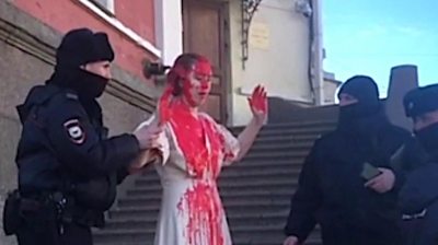 Russian protester covered in fake blood surrounded by police