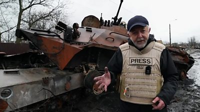 The BBC's Jeremy Bowen in front of armoured vehicle wreckage