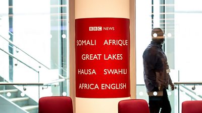 A man walks past a column in New Broadcasting House painted with tv Africa Language services, including Swahili, Somali and Hause.