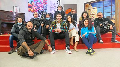 tv Arabic TV team seated together on set smiling at the camera in front of a colourful graffiti mural