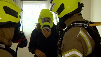Woman being fitted with a smoke hood by firefighters