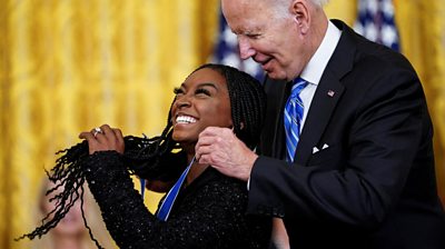 Simone Biles having the Medal of Freedom placed around he neck by President Biden
