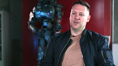 Neill Blomkamp, film director and chief visionary office of Gunzilla Games. He wears a black jacket and brown T-shirt.