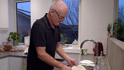 Hans-Erik, a resident of Odensen in Denmark, washes dishes in a sink.