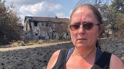 Woman stands infront of burnt out house