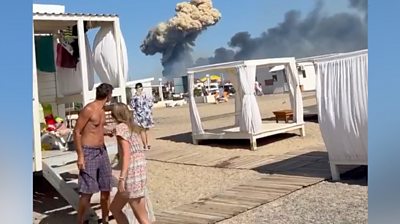 People on beach in Crimea, plume of smoke in background