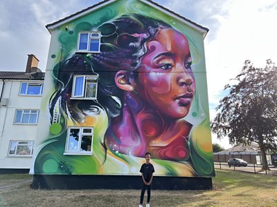 Nylah stands in front of a giant mural of herself on a house