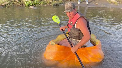 A man riding down the river in a giant pumpkin