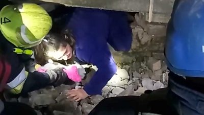 Rescue workers help a girl from a gap in the rubble