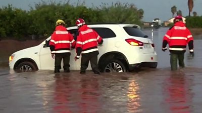 Firefighters standing in flood water near a car in Valencia, Spain