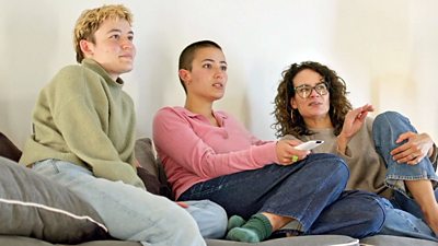 Three people sitting on a sofa watching television