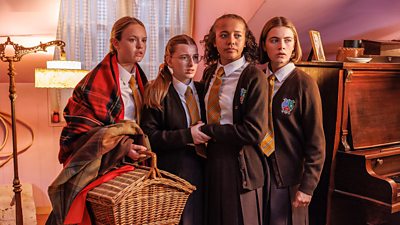 four girls in a Malory Towers uniform looking scared at something offscreen. One is holding a basket
