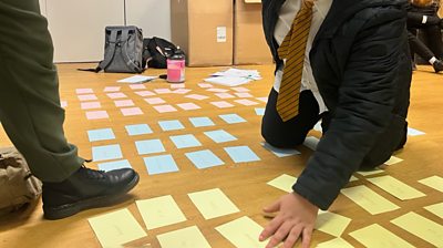 Students engage in a workshop with coloured post it notes scattered on the ground.