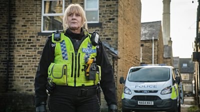 Sarah Lancashire as Catherine Cawood in a mill town standing near a police van