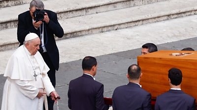 Pope Francis stands as pallbearers carry the coffin of former Pope Benedict