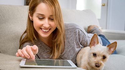 A woman scrolls through her tablet while a small dog looks on