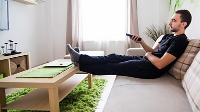 A man lazes on the sofa watching the TV, remote control in hand