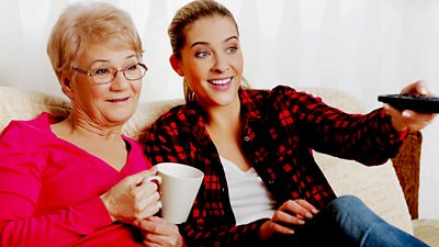 A young woman shows an older woman how to change TV channels