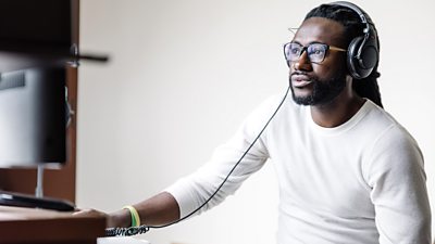 A man listens through headphones at his computer