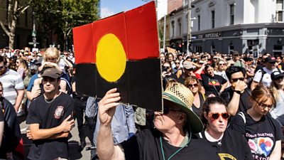 Man holds up a picture of the Aboriginal flag at a protest