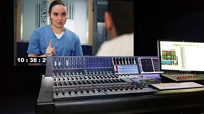 A mixing desk in an edit suite showing a mix of the drama Casualty underway - an episode is on screen behind the desk while the mix is underway.