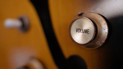 A close up of a volume dial on a wooden musical instrument which is obscured, likely a guitar.