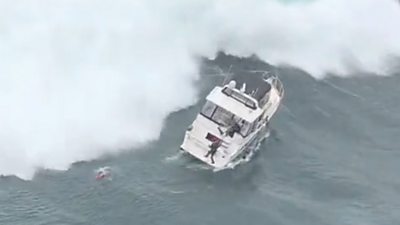 Small boat in rough water with swimmer in sea as big wave about to hit them